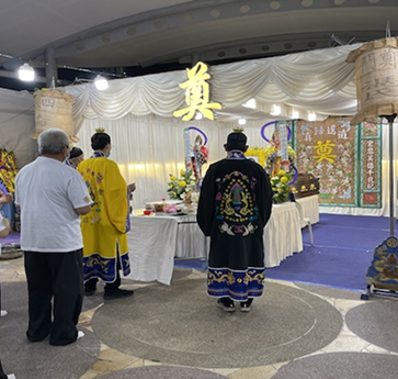 A Buddhist funeral rite in Singapore with a robed priest leading prayers before the family at the altar